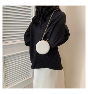 Detail of a white round leather crossbody bag with a gold chain strap on a model