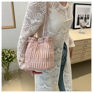 Detail of pink pleated drawstring bucket bag styled with white lace cardigan on model