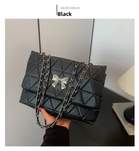 Detail of black quilted crossbody bag featuring a silver bow accent and chain strap