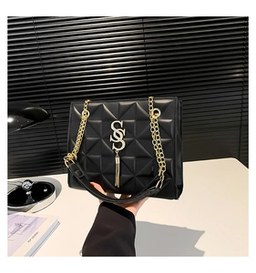 Detail of black quilted shoulder bag with gold chain strap and S-shaped buckle