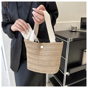 Detail of hand-woven straw tote bag with white canvas handle and metal snap closure