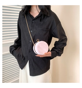 Detail view of pink round evening bag with gold chain strap on a black pleated shirt