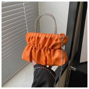 Detail of orange pleated handbag featuring a crystal handle and silver chain strap