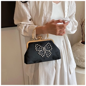 Detail of elegant black satin evening bag with pearl butterfly and gold circular handle
