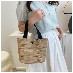 Détail du sac cabas en paille tressée avec poignées en tissu noir et bouton central