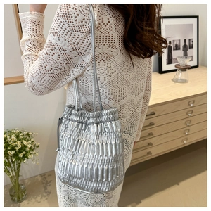 Silver pleated drawstring bucket bag with metallic texture shown on model in studio