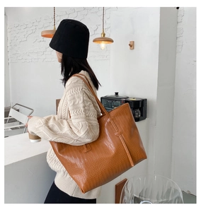 Détail d'un sac cabas marron à motif crocodile porté par un mannequin dans un café