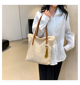 Detailed close-up of woven straw tote bag texture with green tassel and brown straps