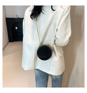 Detail of round black evening clutch with gold chain and handle worn over white blazer