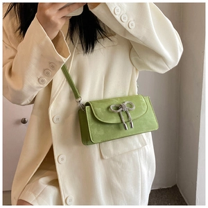 Detail of green shoulder bag featuring sparkling rhinestone bow and metal charms