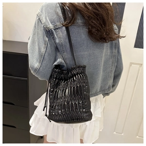 Detailed view of black pleated drawstring bucket bag styled on a female model