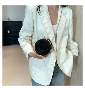 Detail of round black crossbody bag with pleated texture and gold circular handle