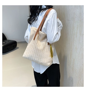 Detailed texture of woven straw tote bag with brown leather strap and yellow tassel accent