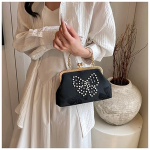 Détail d'un sac à main en satin noir avec papillon en perles et poignée en métal doré