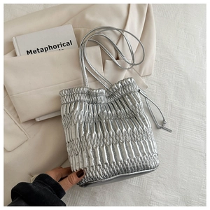 Detail of silver pleated handbag with drawstring closure and metallic finish on cream jacket