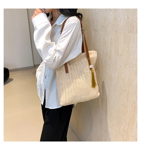 Detail view of woven tote bag with brown leather handles and decorative gold tassel