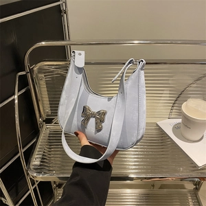 Elegant light blue crescent handbag featuring a large silver metal bow on a modern shelf