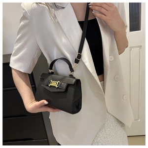 Detail of a chic black crossbody bag with gold woven buckle on a white blazer outfit