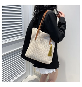 Detail of straw woven tote bag featuring yellow tassels and brown leather shoulder strap