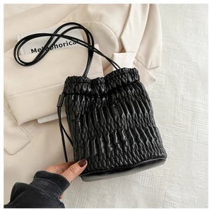 Detail of black pleated drawstring bucket bag texture on a beige suit backdrop