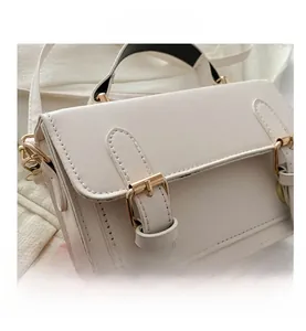 Detail of cream messenger bag showing leather texture and gold buckle hardware
