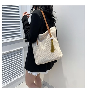 Detail of woven tote bag with V-shaped straw pattern, leather strap and green tassel charm
