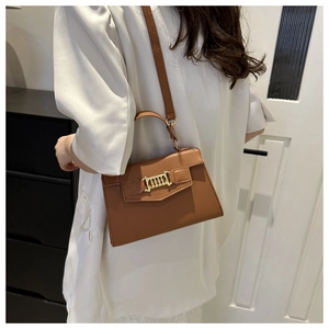 Brown faux leather crossbody bag with gold chain detail worn by a model in casual setting