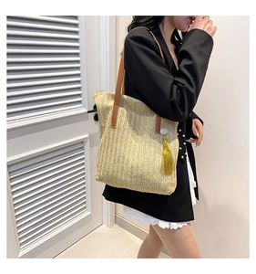 Detail of woven straw tote bag featuring brown leather straps and yellow pearl tassel