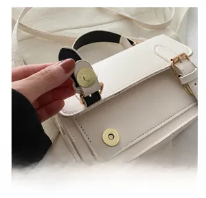 Detail of the golden magnetic buckle closure on a beige faux leather crossbody bag