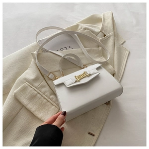 Detail view of white square crossbody bag with gold chain lock on beige blazer