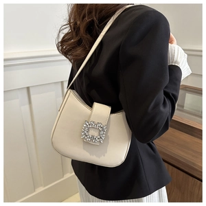 Détail d'un sac baguette beige avec boucle de luxe en cristal porté à l'épaule