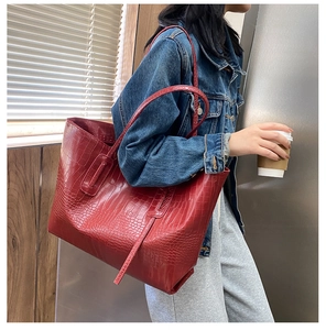 Détail d'un sac cabas rouge avec gaufrage crocodile porté à l'épaule par un mannequin