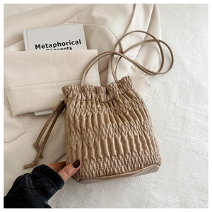 Detail of a beige pleated leather bucket bag with drawstring and fine shoulder strap