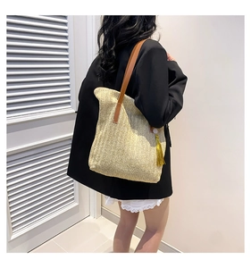 Detail view of hand-woven straw tote with brown leather straps and yellow tassel