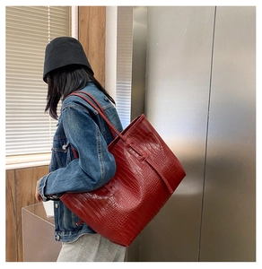 Détail d'un grand sac cabas rouge à motif crocodile porté à l'épaule par un mannequin