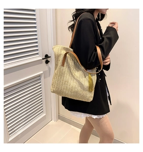 Detail of woven straw tote bag featuring brown leather handles and gold tassel charm