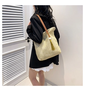 Close-up of beige woven bucket bag featuring brown leather strap and yellow tassel detail