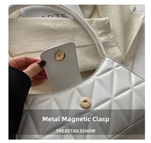 Detalle del cierre magnético dorado en el bolso baguette blanco con diseño acolchado