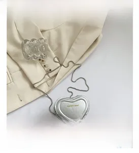 Detail view of mini heart-shaped silver handbag with snake chain on a beige blazer
