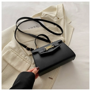 Detail of black crossbody bag with gold chain buckle on a cream blazer background