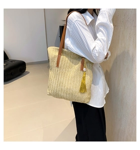 Detail of handwoven straw tote bag with brown leather straps and yellow tassel accessory