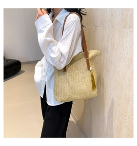Detail of hand-woven straw shoulder bag featuring a brown leather strap and stylish tassel