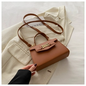Flat lay of brown leather square crossbody bag with gold chain buckle on blazer