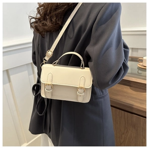 Detail of a vintage beige square crossbody bag with gold buckles worn by a model