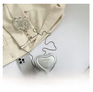 Detail of silver heart-shaped mini bag with chain strap and gold lettering on white base