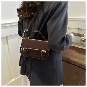 Detail of dark brown leather messenger bag featuring gold buckles on a stylish crossbody