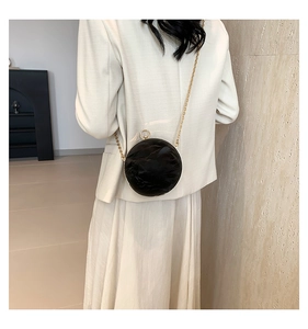 Detail of black pleated round crossbody bag with golden chain and metallic buckle
