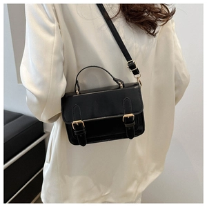 Detail of a black leather retro satchel bag with gold hardware worn over a white blazer