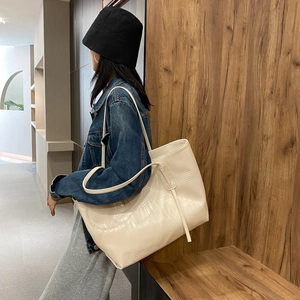 Sac cabas beige à motif crocodile porté par un mannequin dans un décor minimaliste