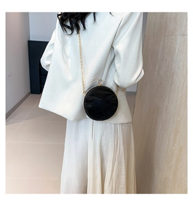 Model wearing a black round pleated leather crossbody bag with a gold chain and ring clasp